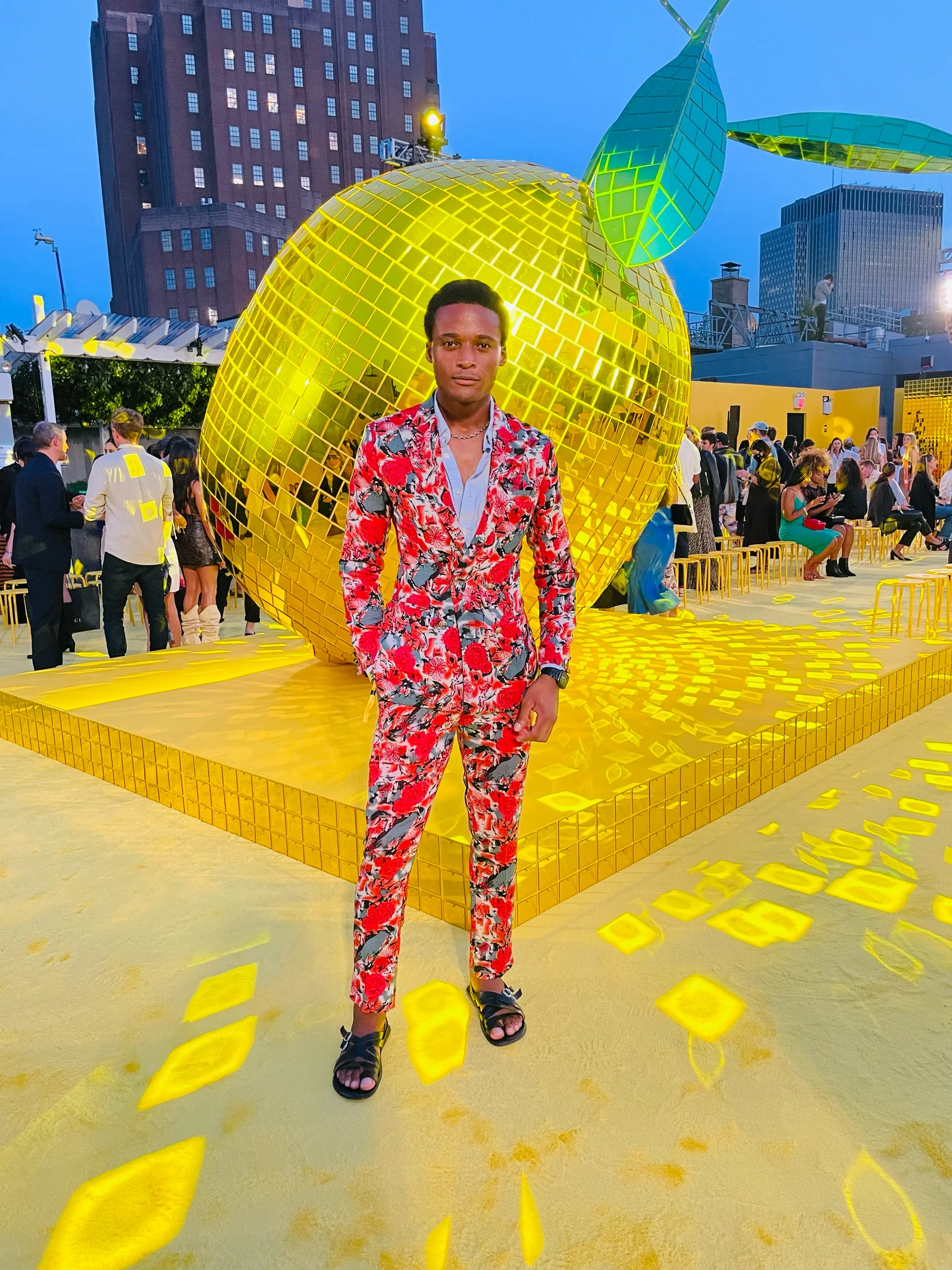 Kudzai King in a patterned red suit beside a yellow event installation.