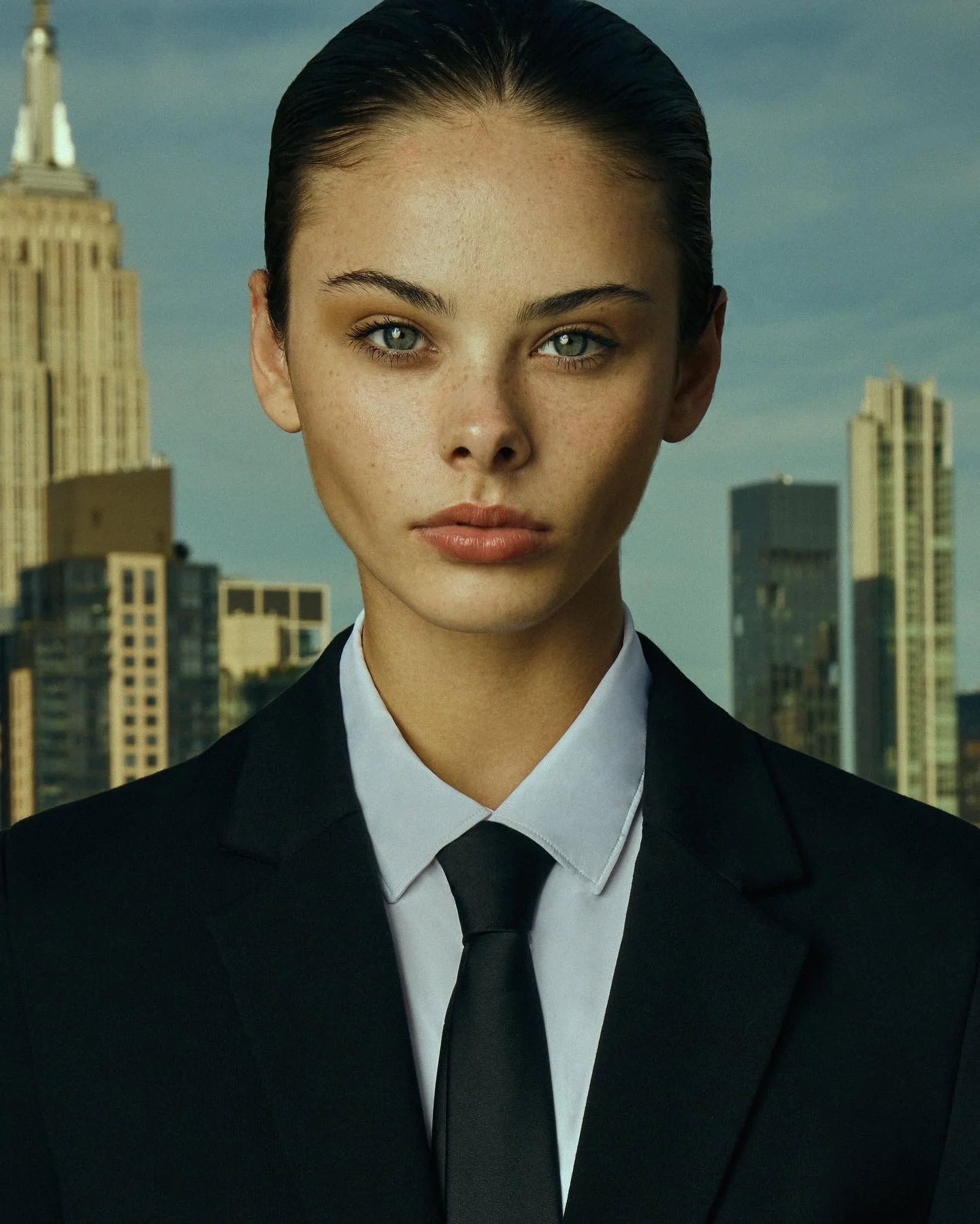 A close portrait in black tailoring with the New York skyline behind.