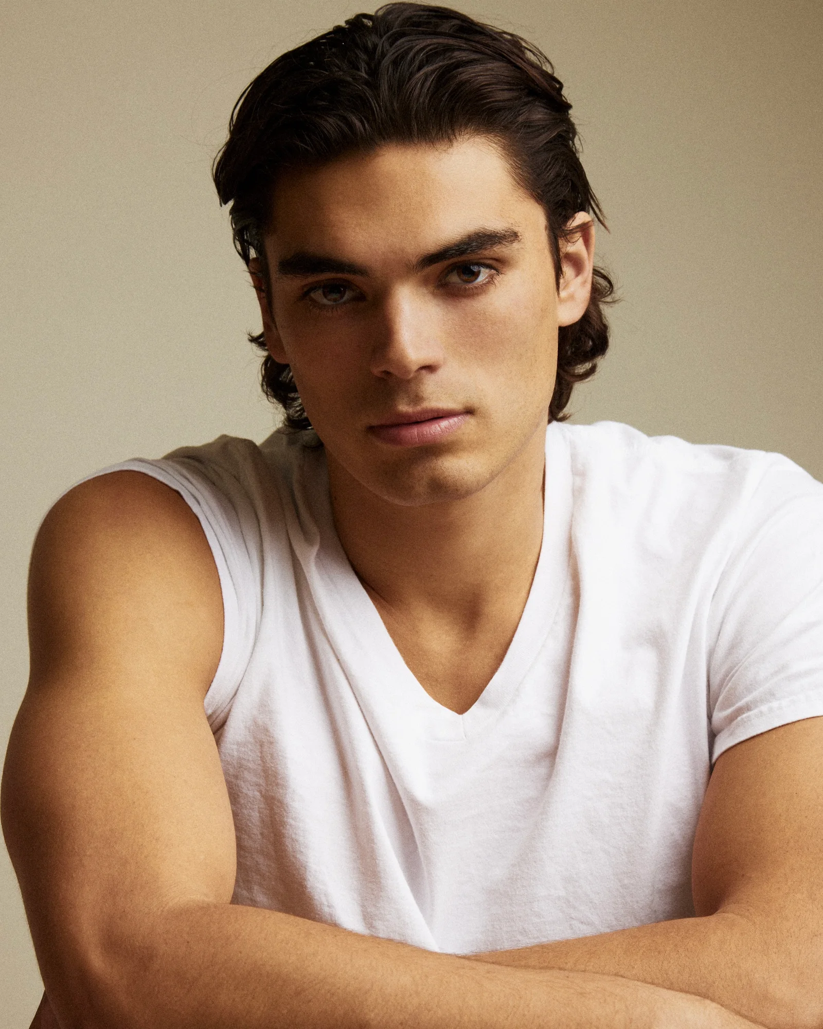 A seated portrait of a model wearing a white T-shirt against a warm neutral background.