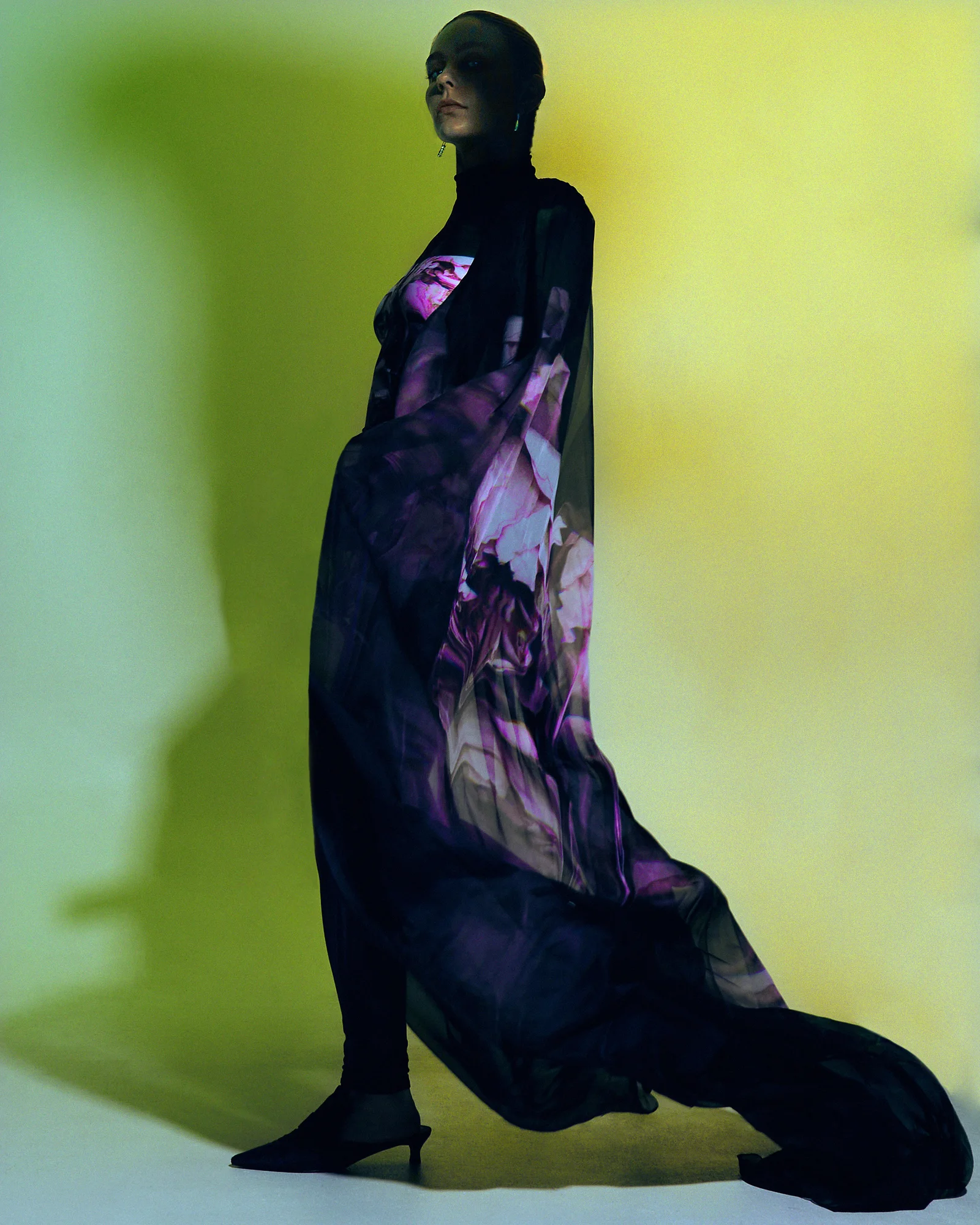 A model in a flowing purple patterned dress against a green background.