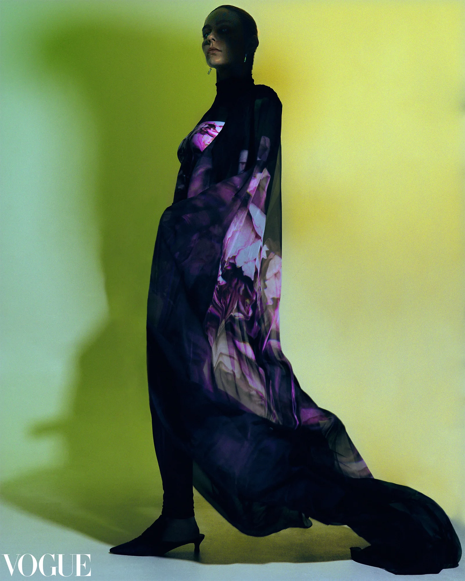 A model in a purple patterned dress against green with a Vogue masthead in the supplied image.