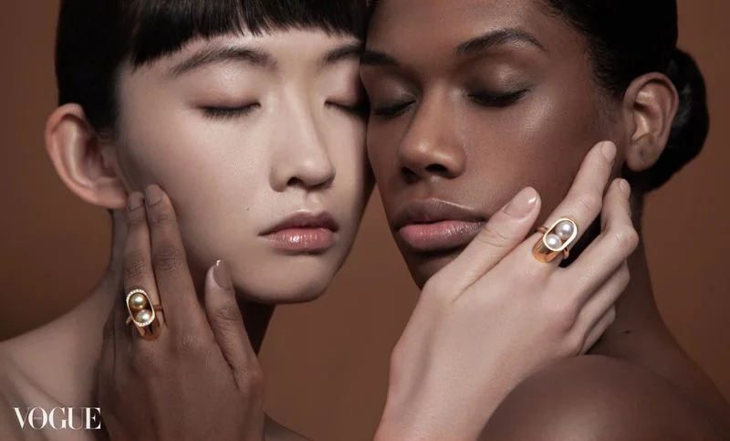 A beauty photograph of two models with eyes closed, jewellery and hands framing their faces.