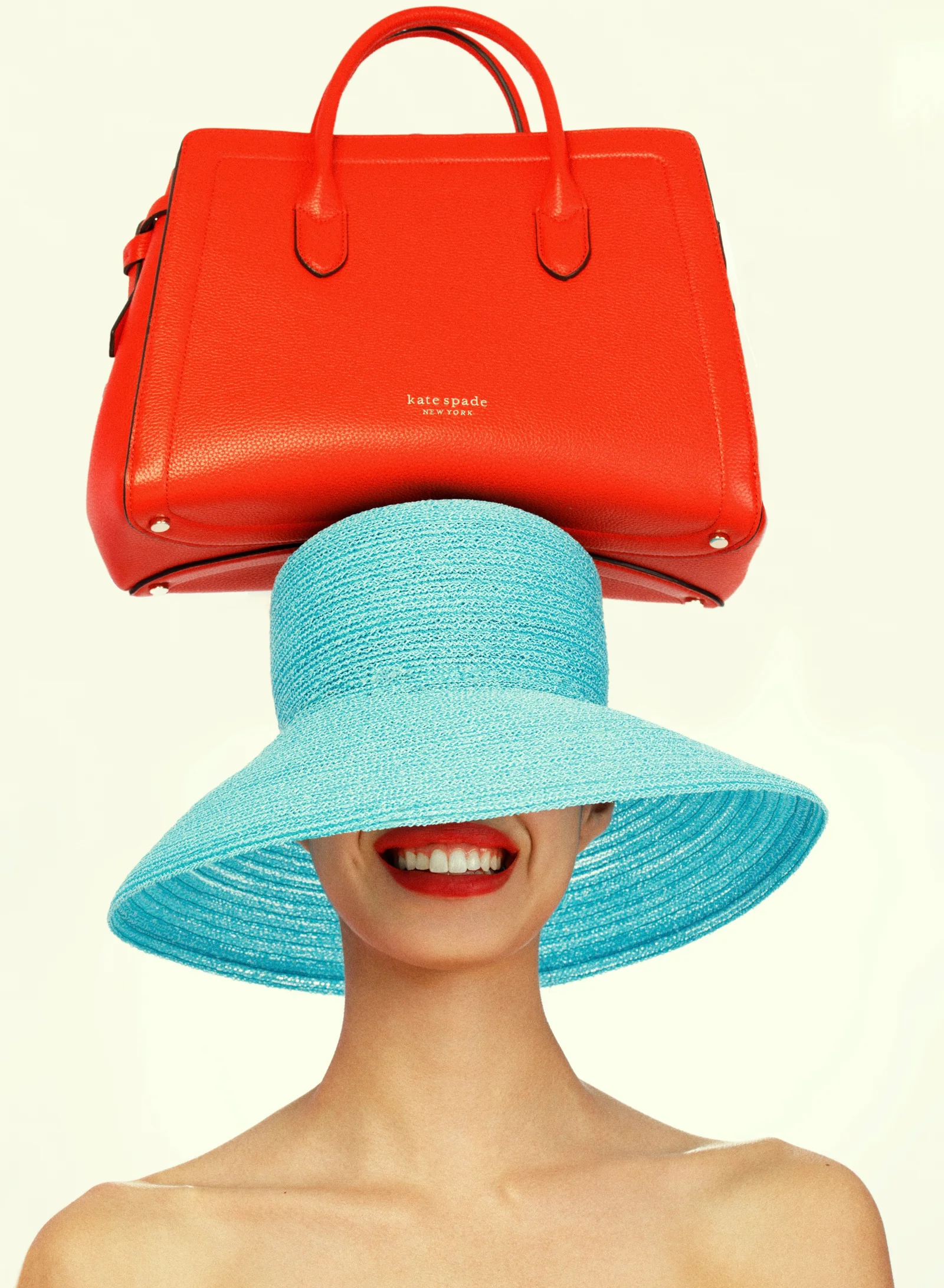 A bright red handbag balanced above a blue hat hiding a smiling face.