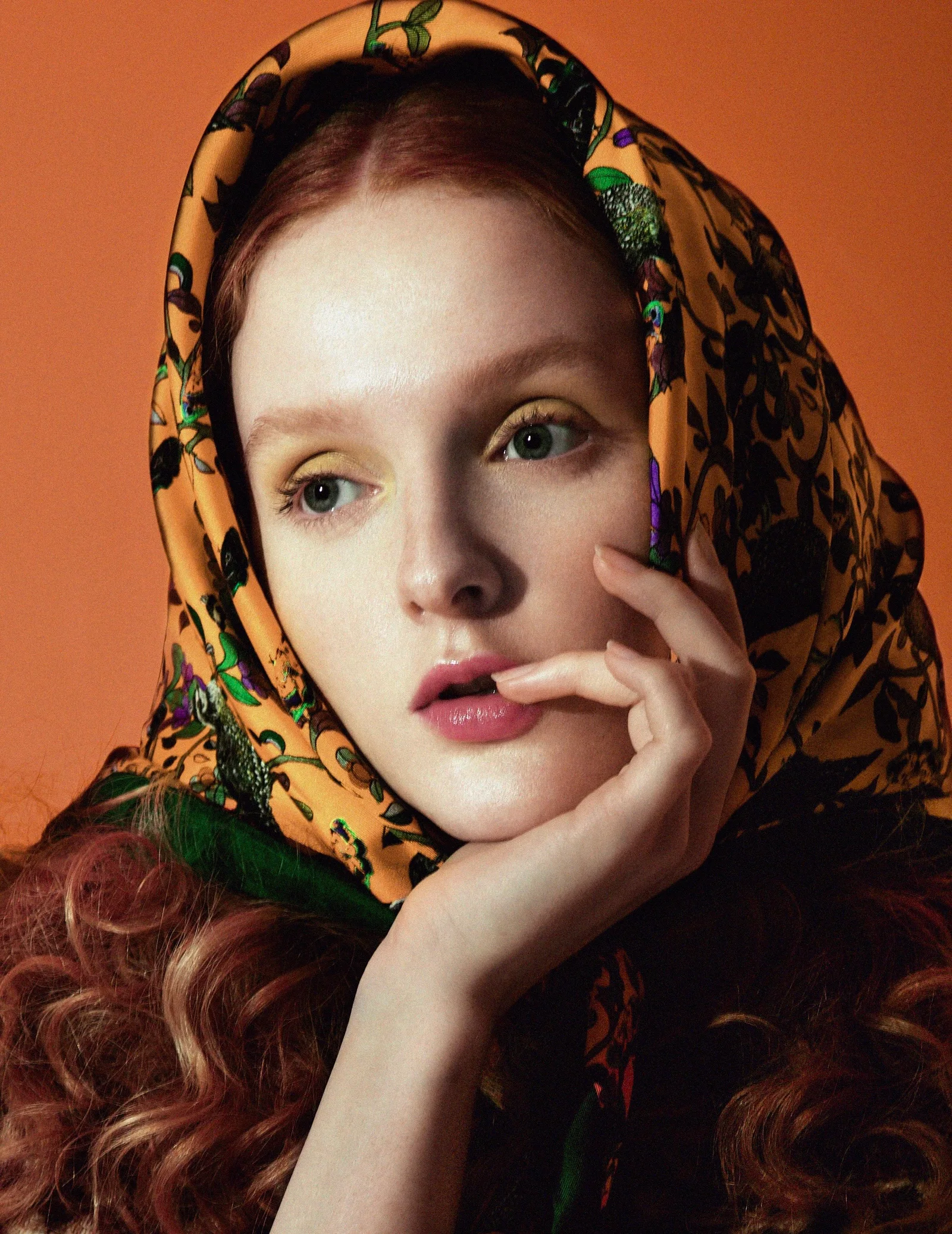 A close portrait with a patterned scarf against an orange studio background.
