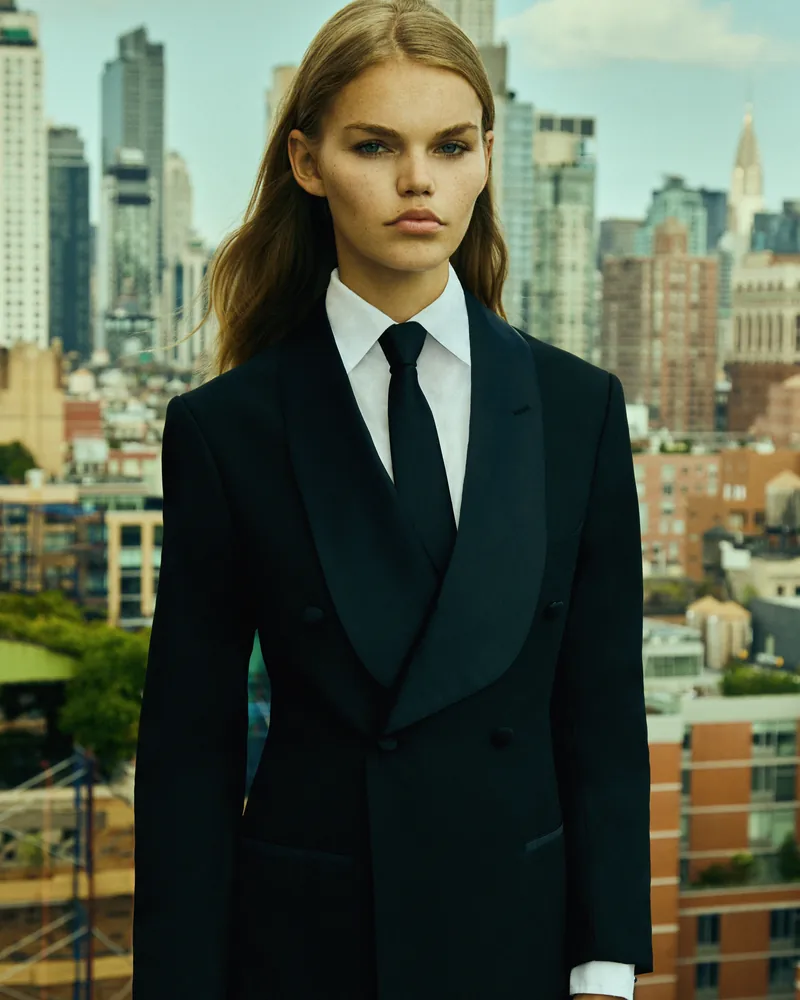 A model in black tailoring on a rooftop with the New York skyline behind her.